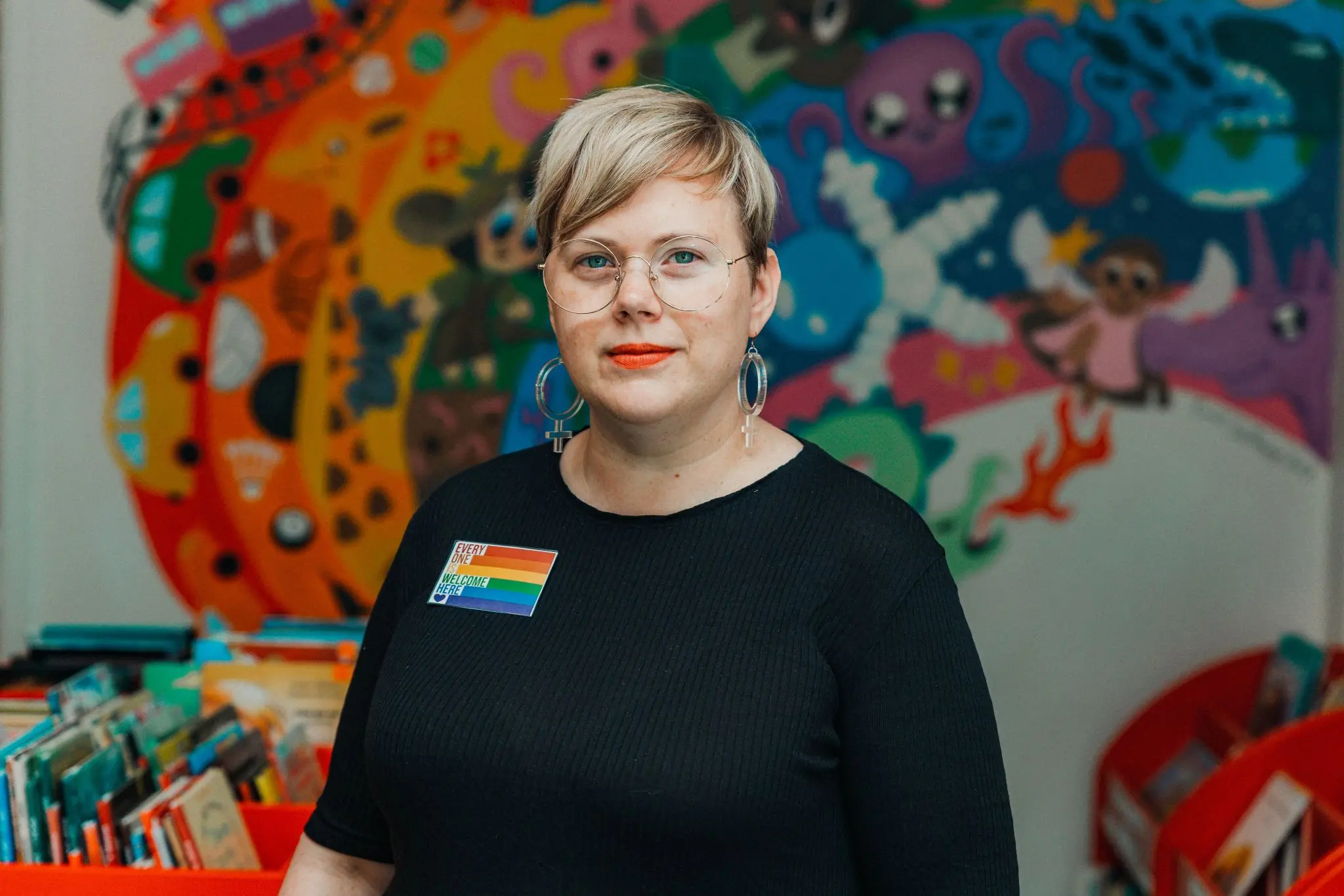 Mimmi Söderlund står framför en färgglatt målad vägg, regnbågsbibliotikarie