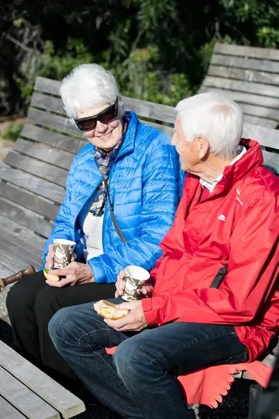 Äldre par dricker kaffe i solen.