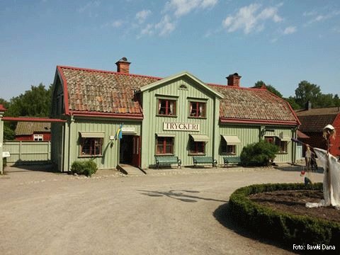 Gamla tryckeribyggnaden på Vallby friluftsmuseum. Grön gammal träbyggnad med rött tegeltak.