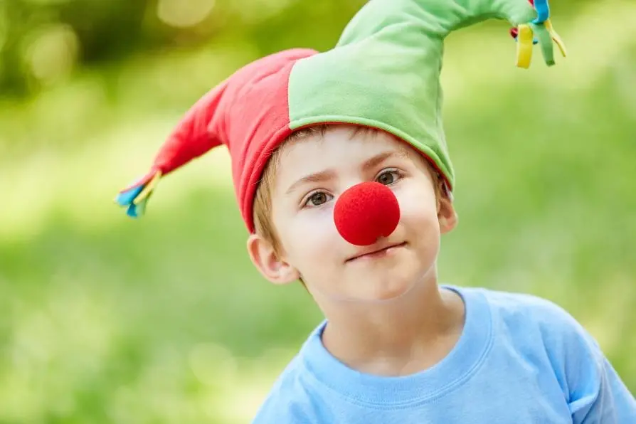 ett barn med narrmössa och röd boll som näsa