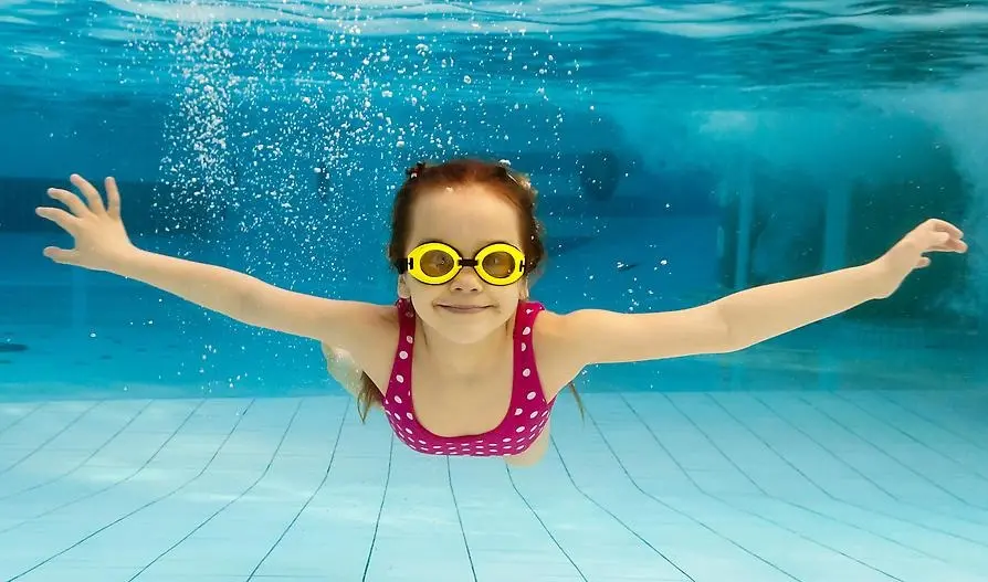 Ett barn med simglasögon som simmar under vattnet i en swimmingpool.