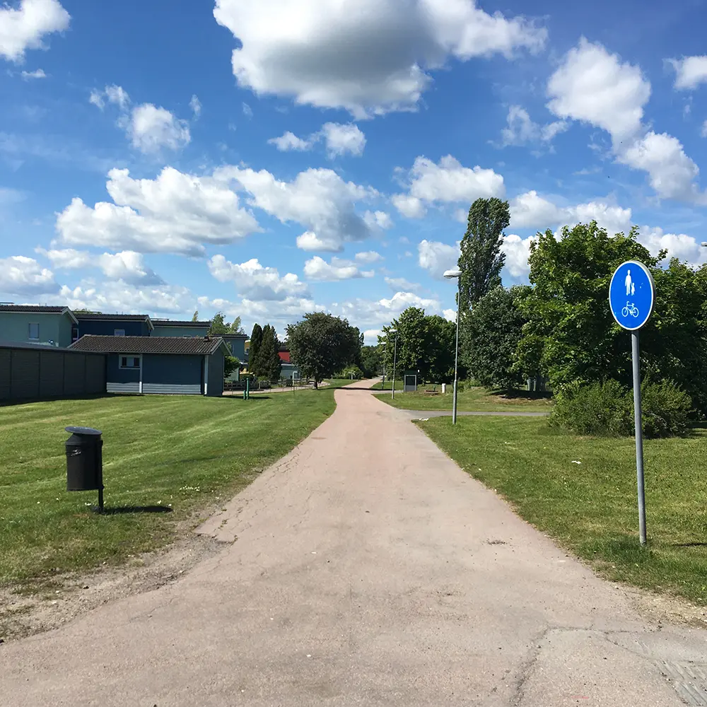 Foto på en cykelbana en fin sommardag med blå himmel och lätta moln. Bredvid finns grönt gräs, en papperskorg och vägskylt för cykelbana.