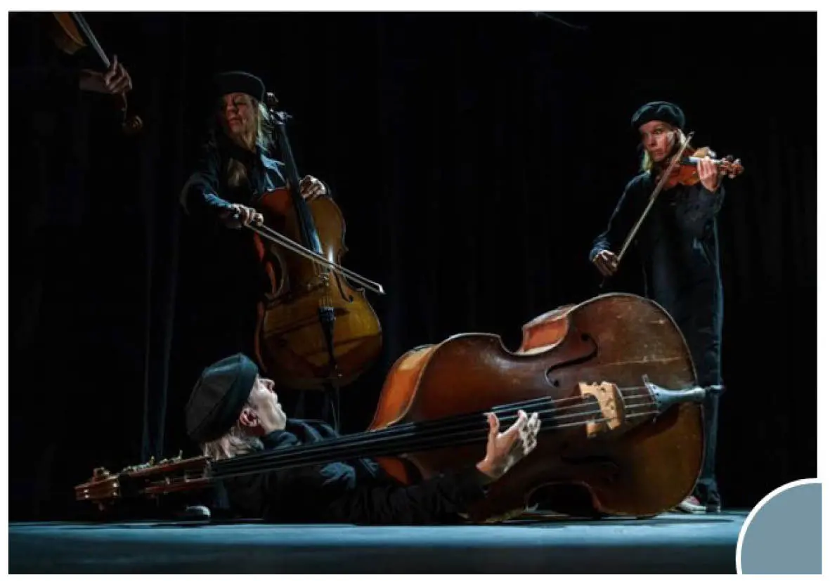 En mörk scen, med tre personer med olika stråkinstrument. En ligger på golvet och spelar kontrabas, en sitter och spelar cello och en står och spelar fiol.