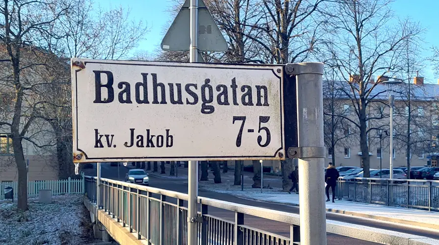 Skylt på stolpe med gatan och kvarterets namn med texten Badhusgatan 7-5 kv. Jakob