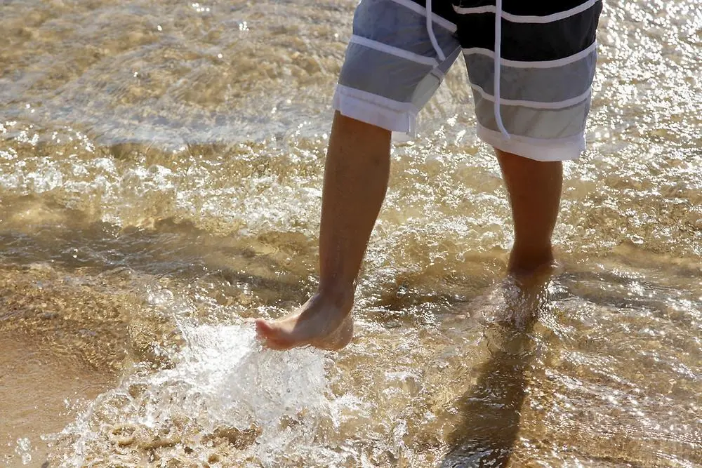 Nakna barnfötter plaskar i vattnet på en sandstrand