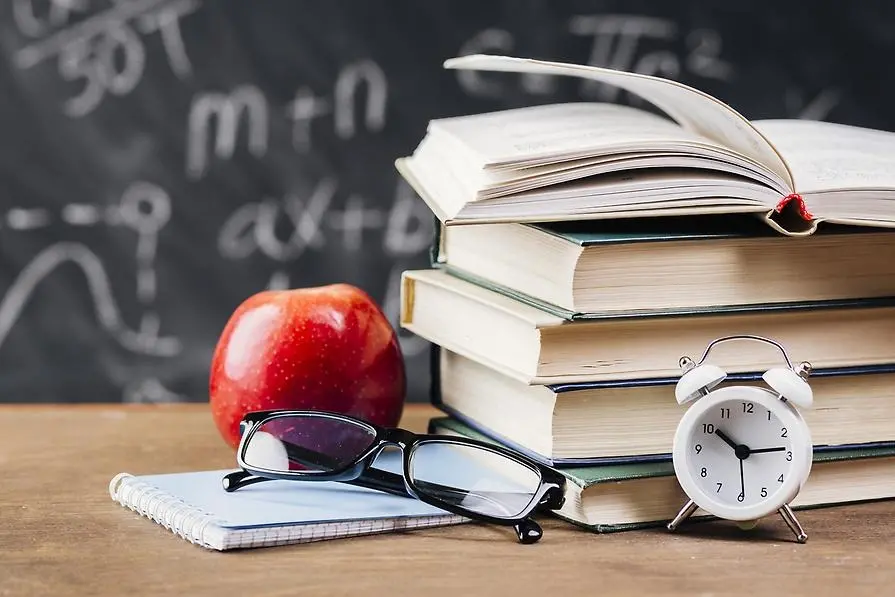Lärares skrivbord med böcker, glasögon, klocka och äpple