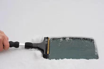 Hand som skrapar en snötäckt bilruta med en snöskrapa.