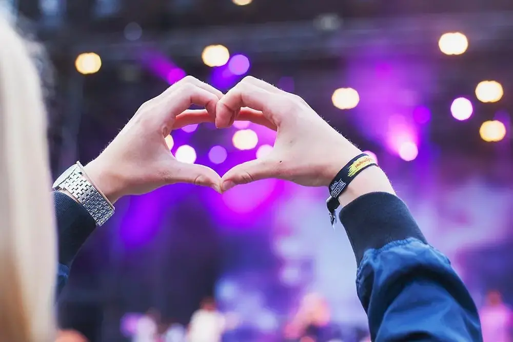 Två händer i formen av ett hjärta, framför en scen.