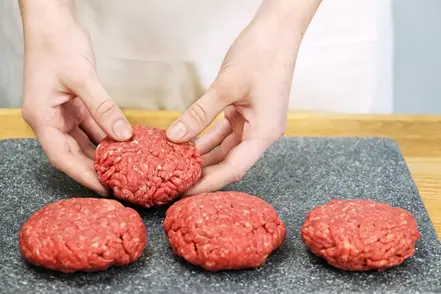 Råa hamburgare formas av två händer.